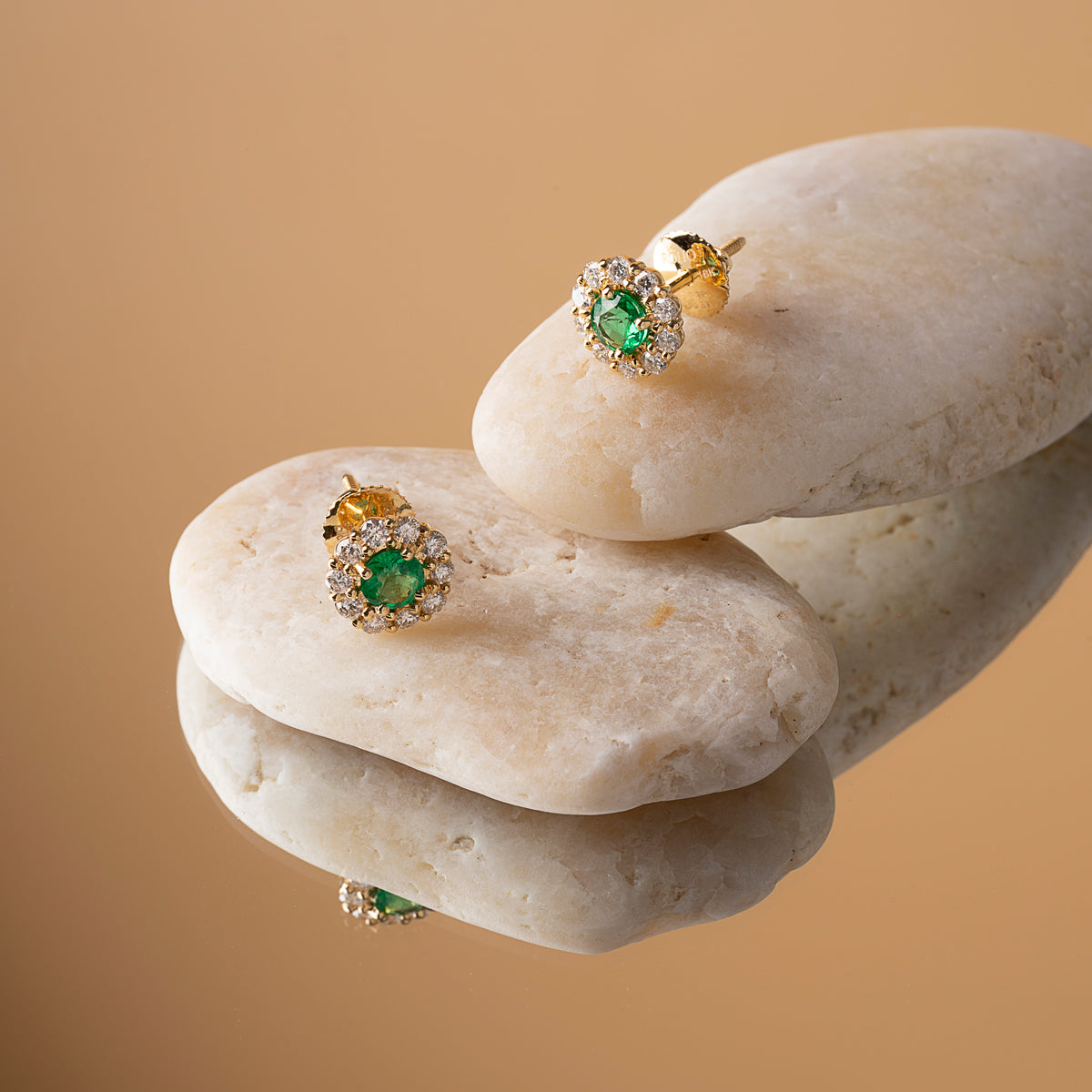 Emerald and diamond halo stud earrings in 18K yellow gold on a pale stone