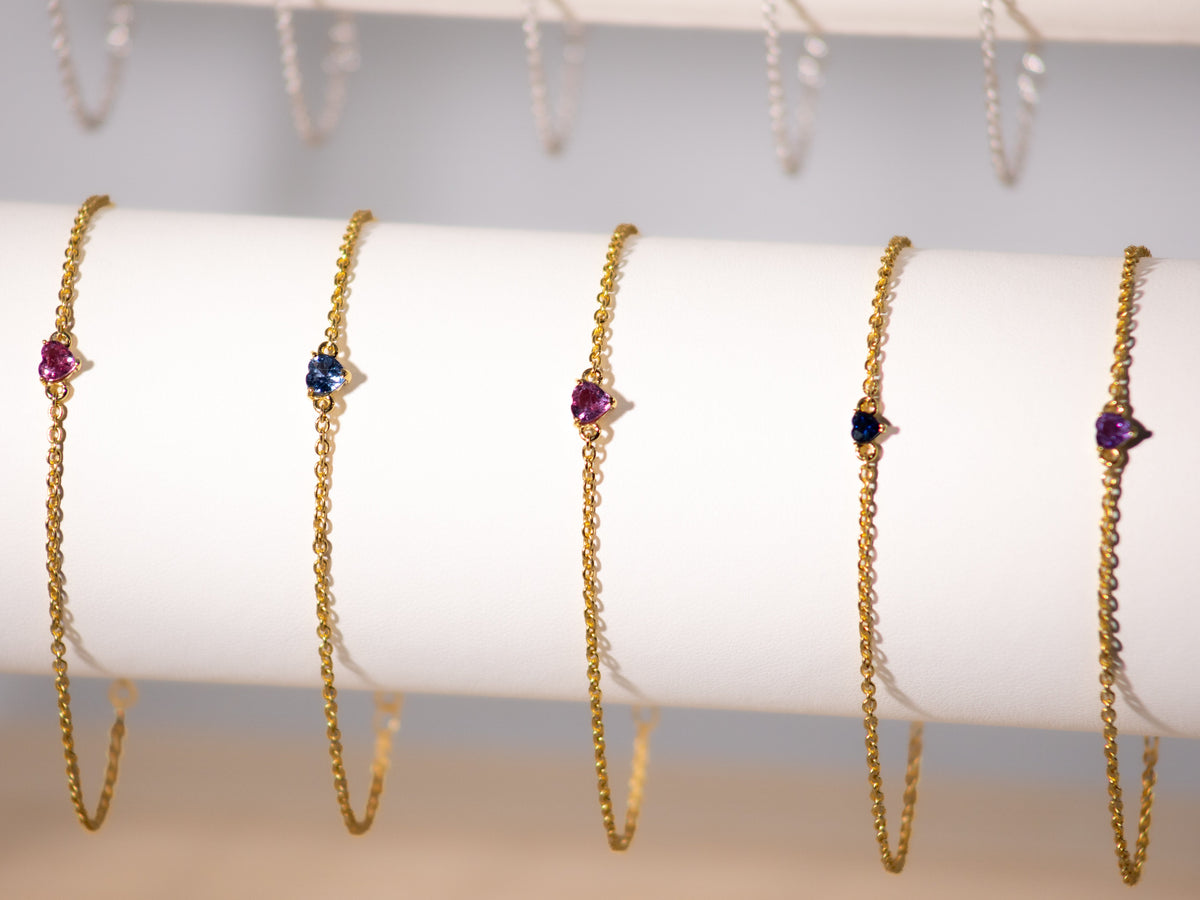 Pink and blue sapphire heart bracelets in 925 sterling silver with yellow gold finish on a display