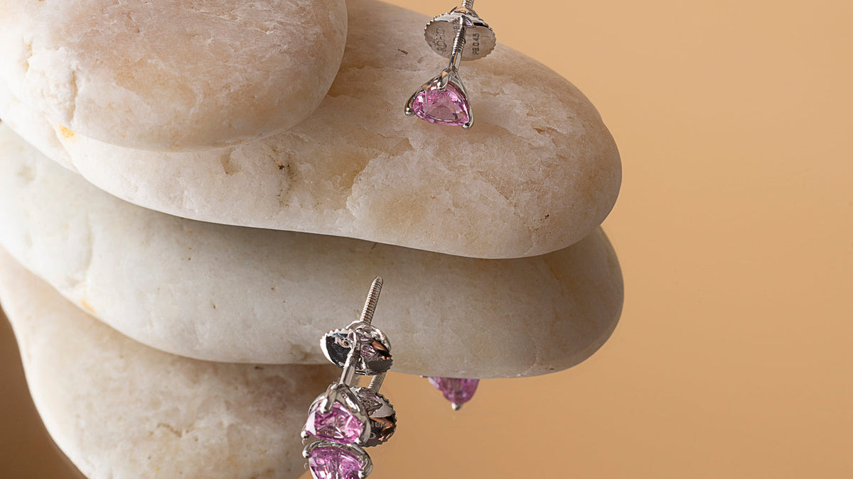 Natural pink sapphire heart stud earrings in 18K gold on stacked white pebbles