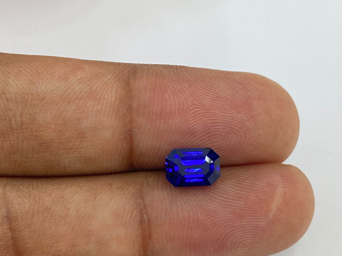 Natural royal blue emerald-cut sapphire held between two fingers