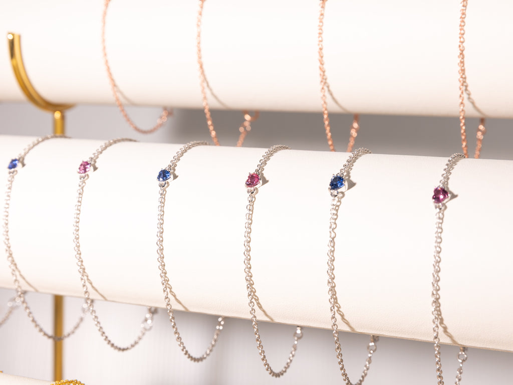 Pink and blue sapphire heart bracelets in 925 sterling silver with rose gold and white rhodium finish on a display