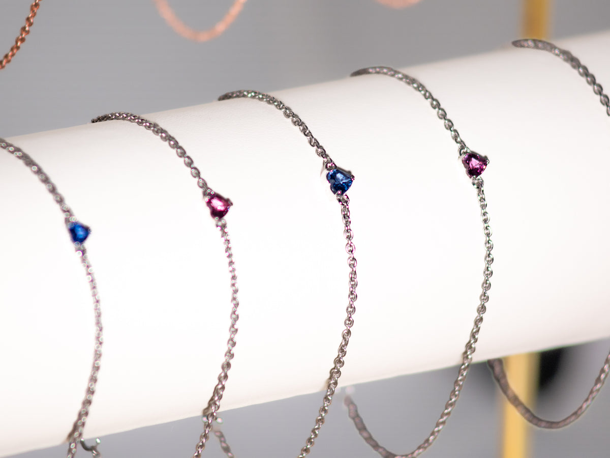 Sapphire heart bracelets in white rhodium and rose gold finishes on a display