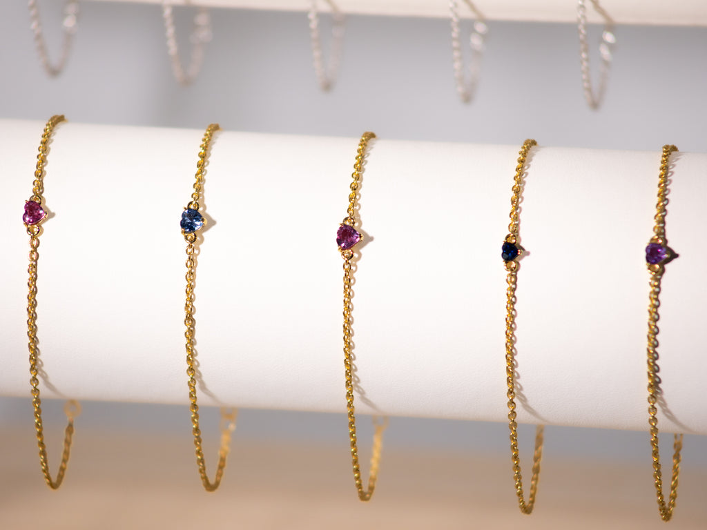 Pink and blue sapphire heart bracelets in 925 sterling silver with yellow gold finish on a display