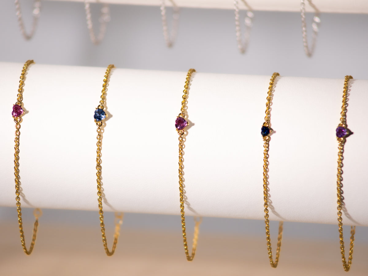 Pink and blue sapphire heart bracelets in 925 sterling silver with yellow gold finish on a display