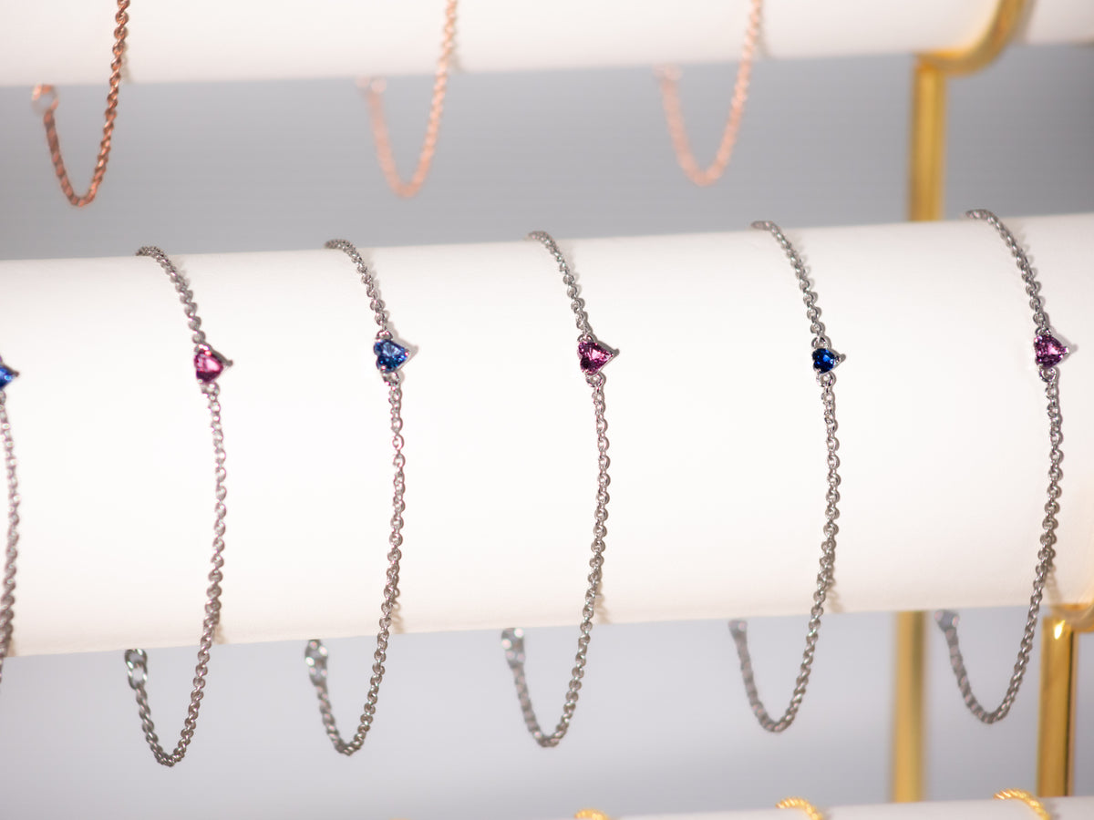 Pink and blue sapphire heart bracelets in 925 sterling silver with white rhodium finish on a display