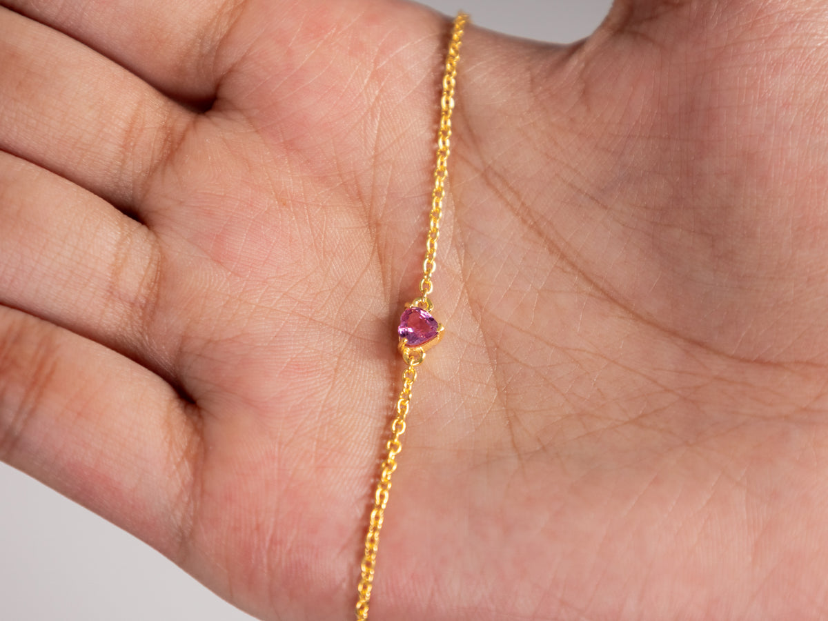 Pink sapphire heart bracelet held in the palm to show its dainty size