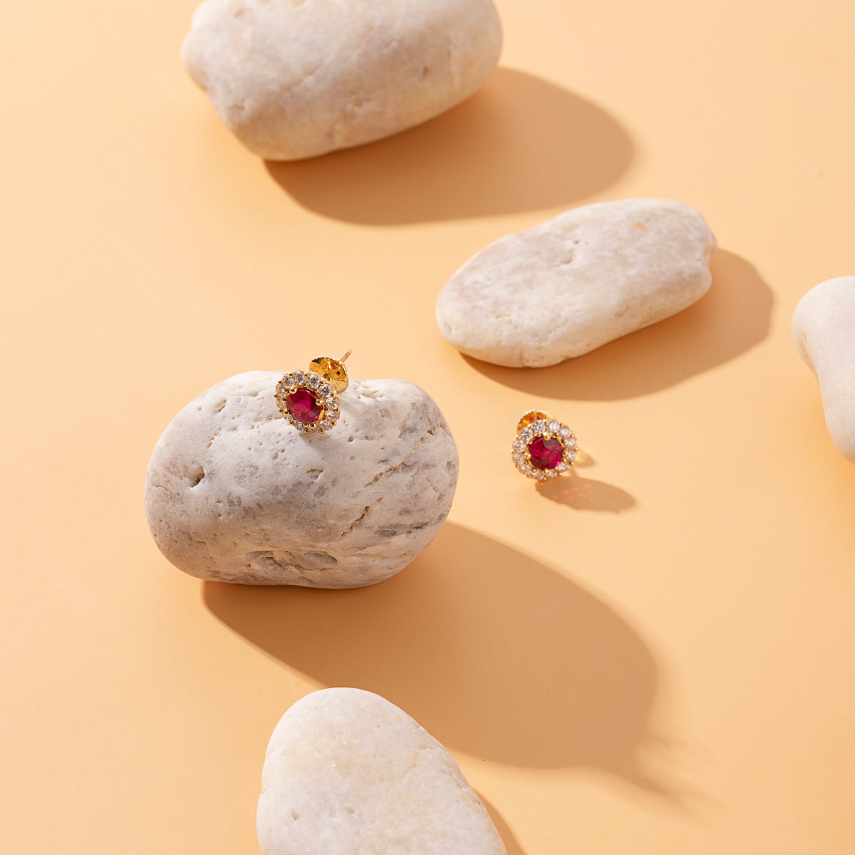 Ruby and diamond halo stud earrings in 18K gold on a pale stone