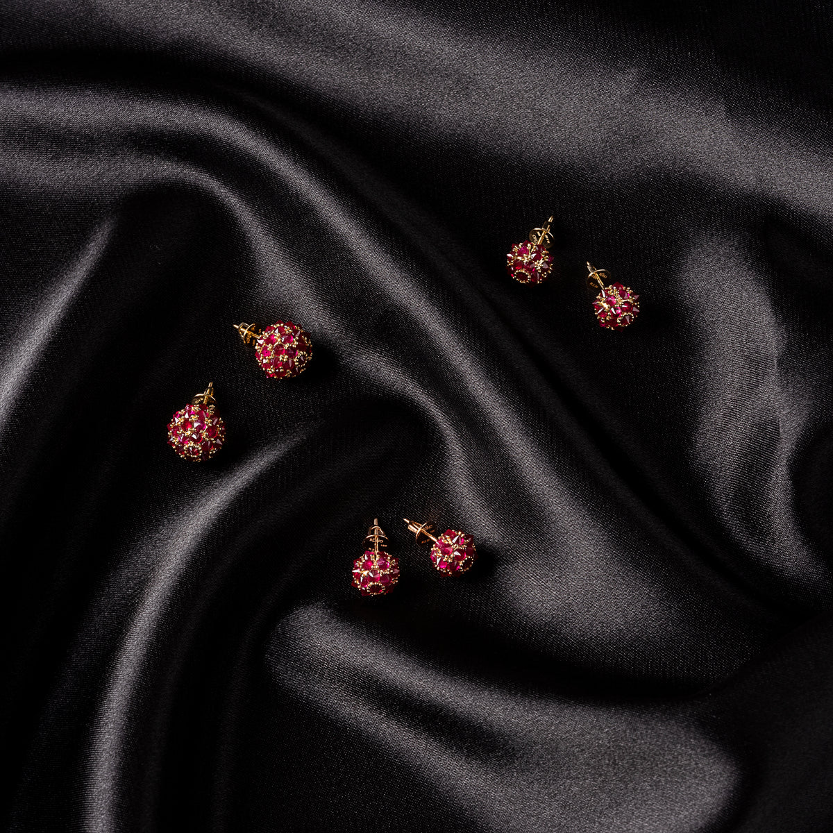 Three pairs of natural ruby spike ball stud earrings in 18K gold on black satin