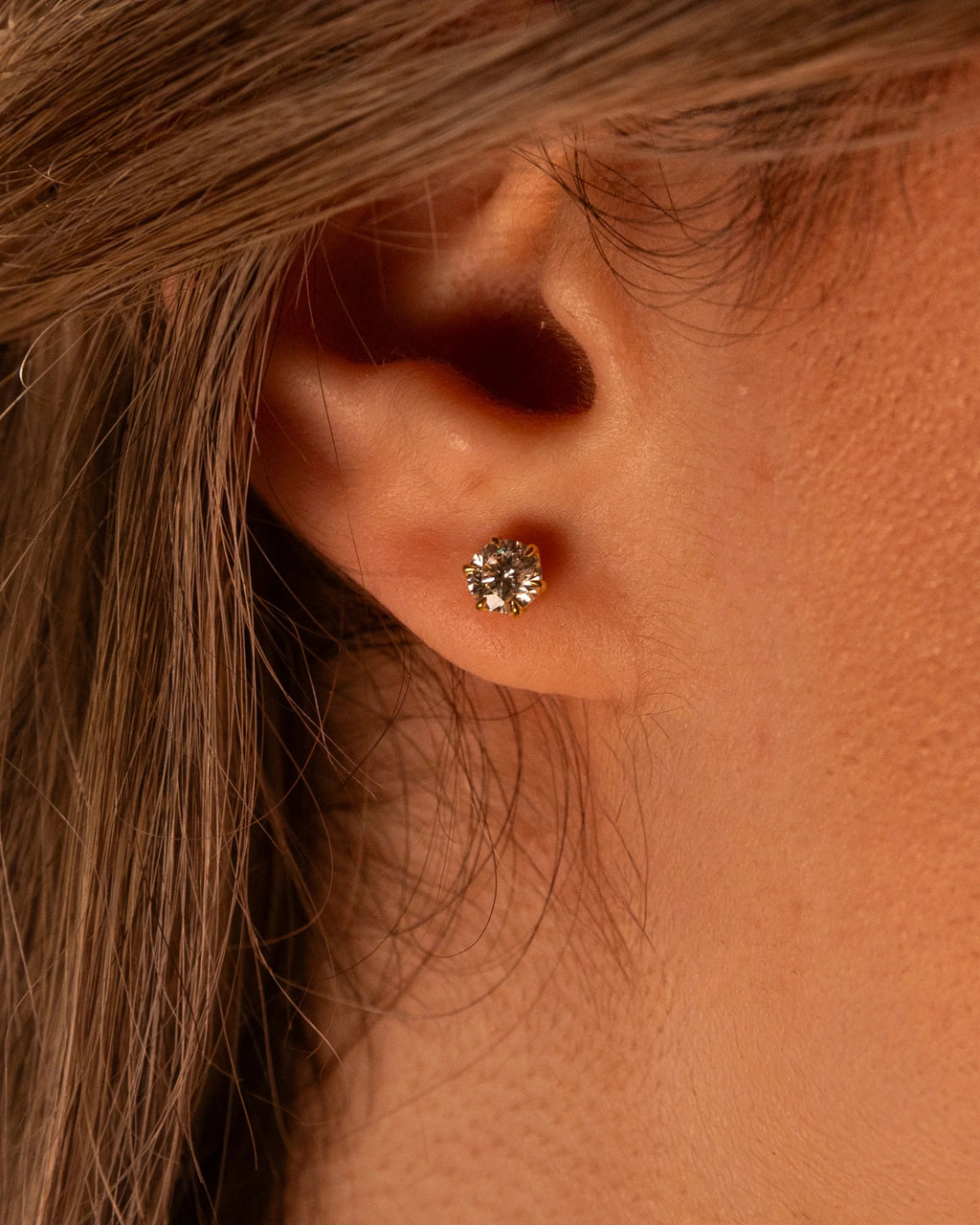 Six-prong yellow gold plated diamond stud on the ear in warm light