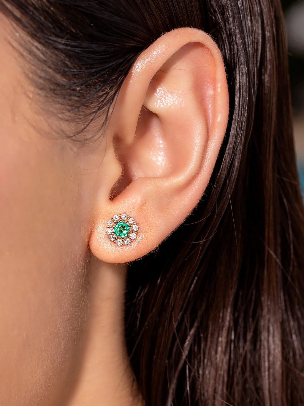Zambian emerald and diamond halo stud earring in 18K gold, worn on the ear