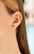Blue sapphire stud earring worn on the ear, with long hair behind the shoulder