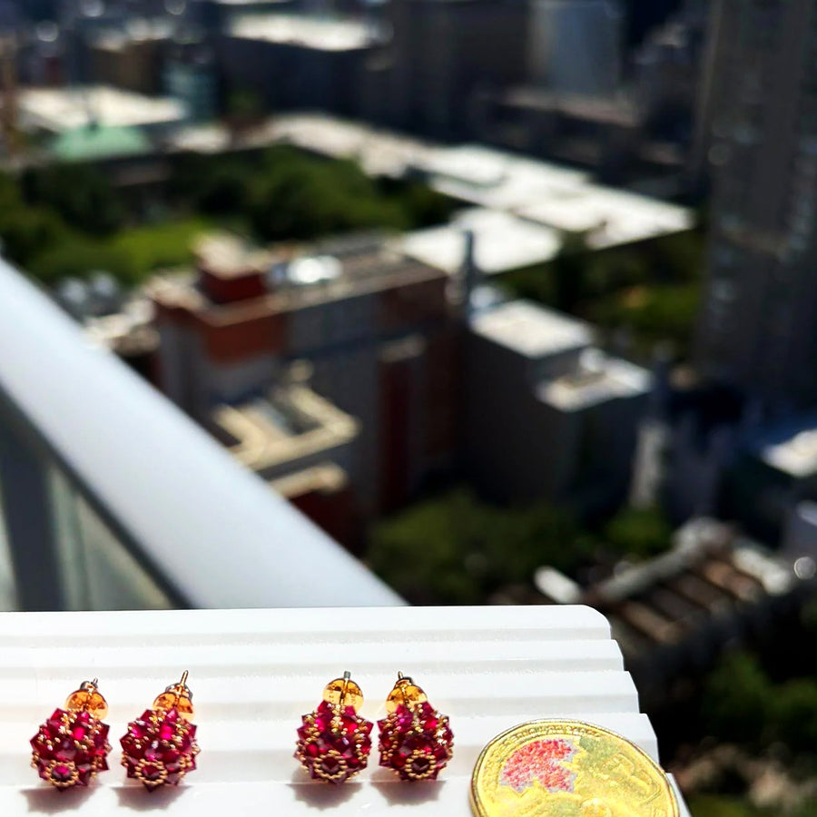 Ruby spike ball stud earrings in 18K gold on a white display stand