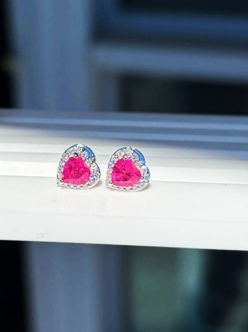 Pink sapphire and diamond heart halo stud earrings in 18K white gold on a white display stand