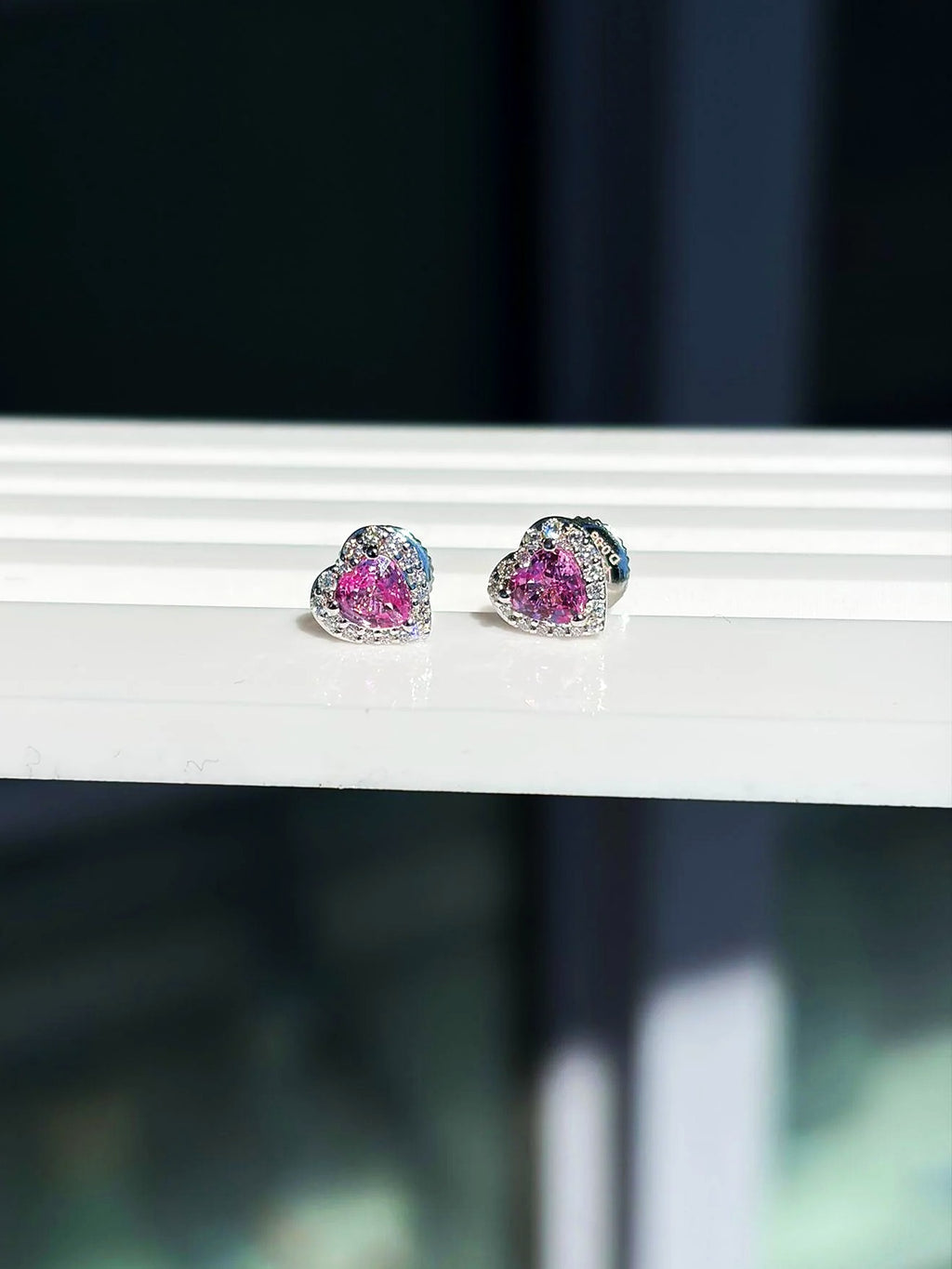 Pendientes de botón pequeños de corazón con zafiro rosa y diamantes en oro blanco de 18K sobre un expositor blanco