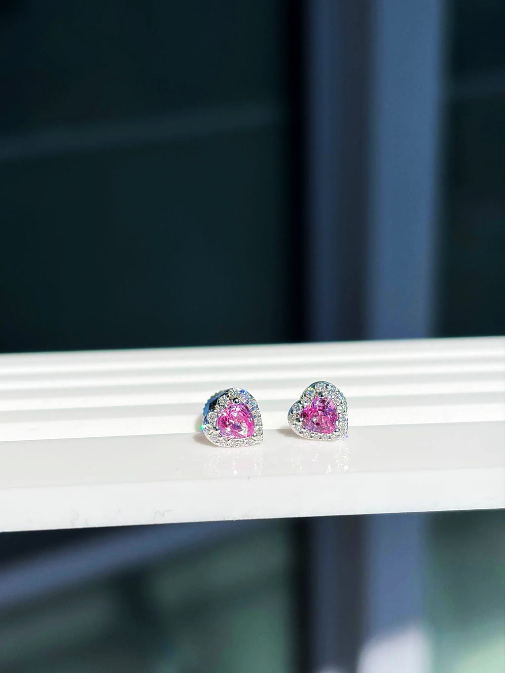 Pendientes de botón pequeños de corazón con zafiro rosa y diamantes en oro blanco de 18K sobre un expositor blanco