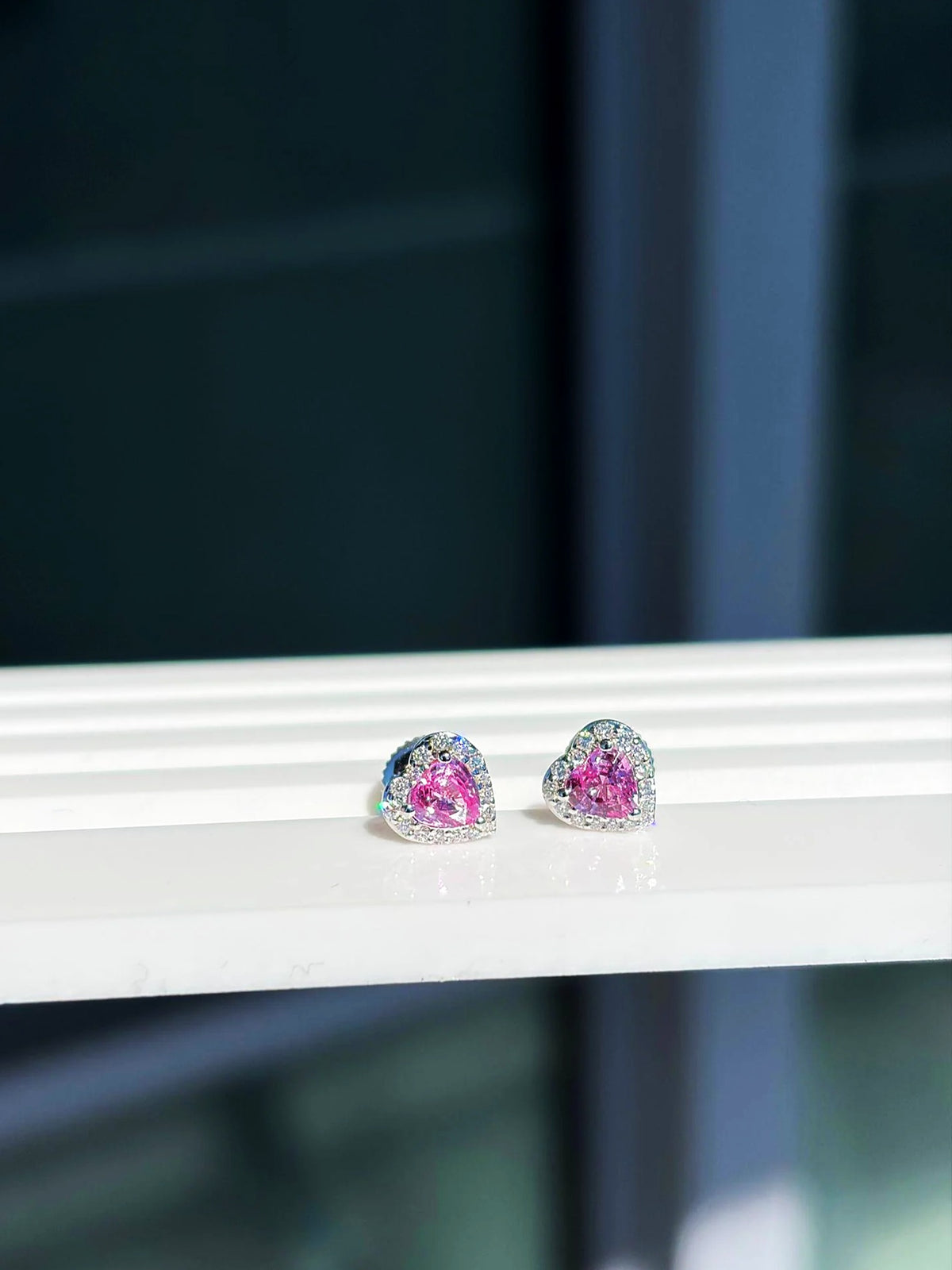 Pendientes de botón pequeños de corazón con zafiro rosa y diamantes en oro blanco de 18K sobre un expositor blanco
