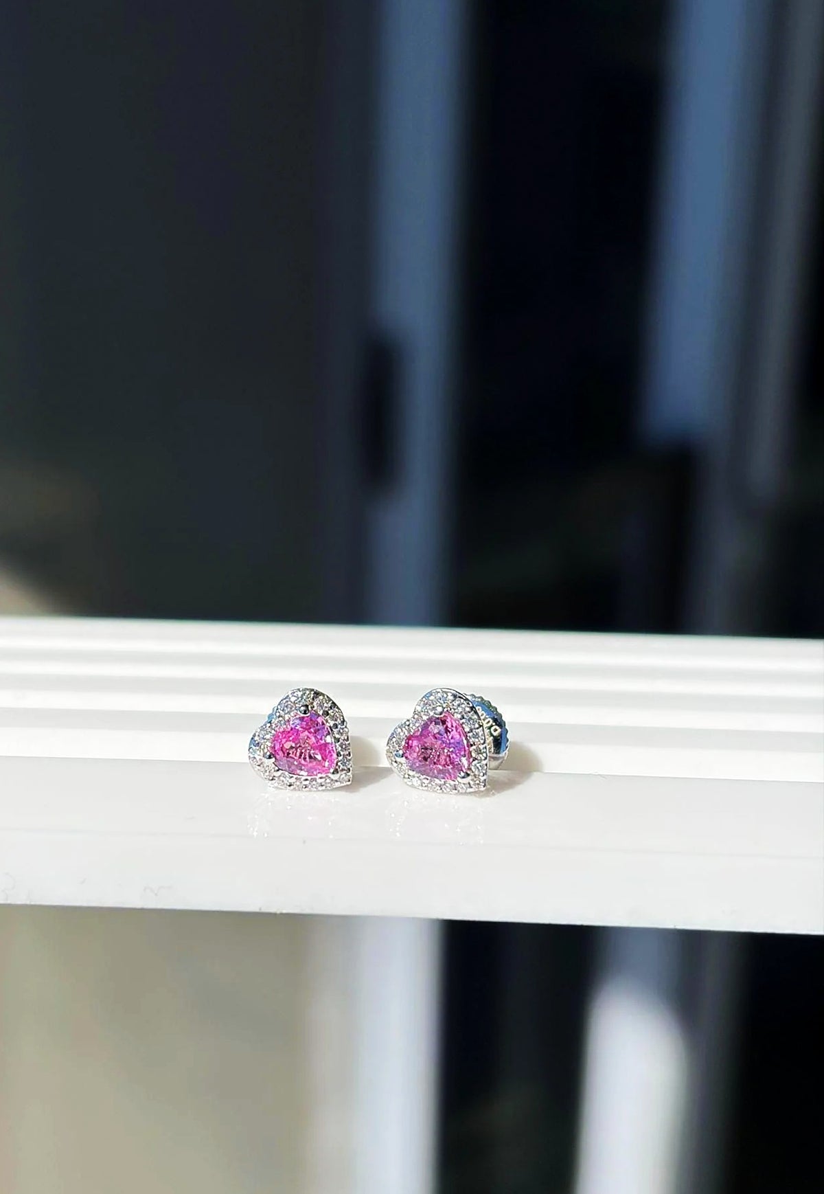 Pendientes de botón pequeños de corazón con zafiro rosa y diamantes en oro blanco de 18K sobre un expositor blanco