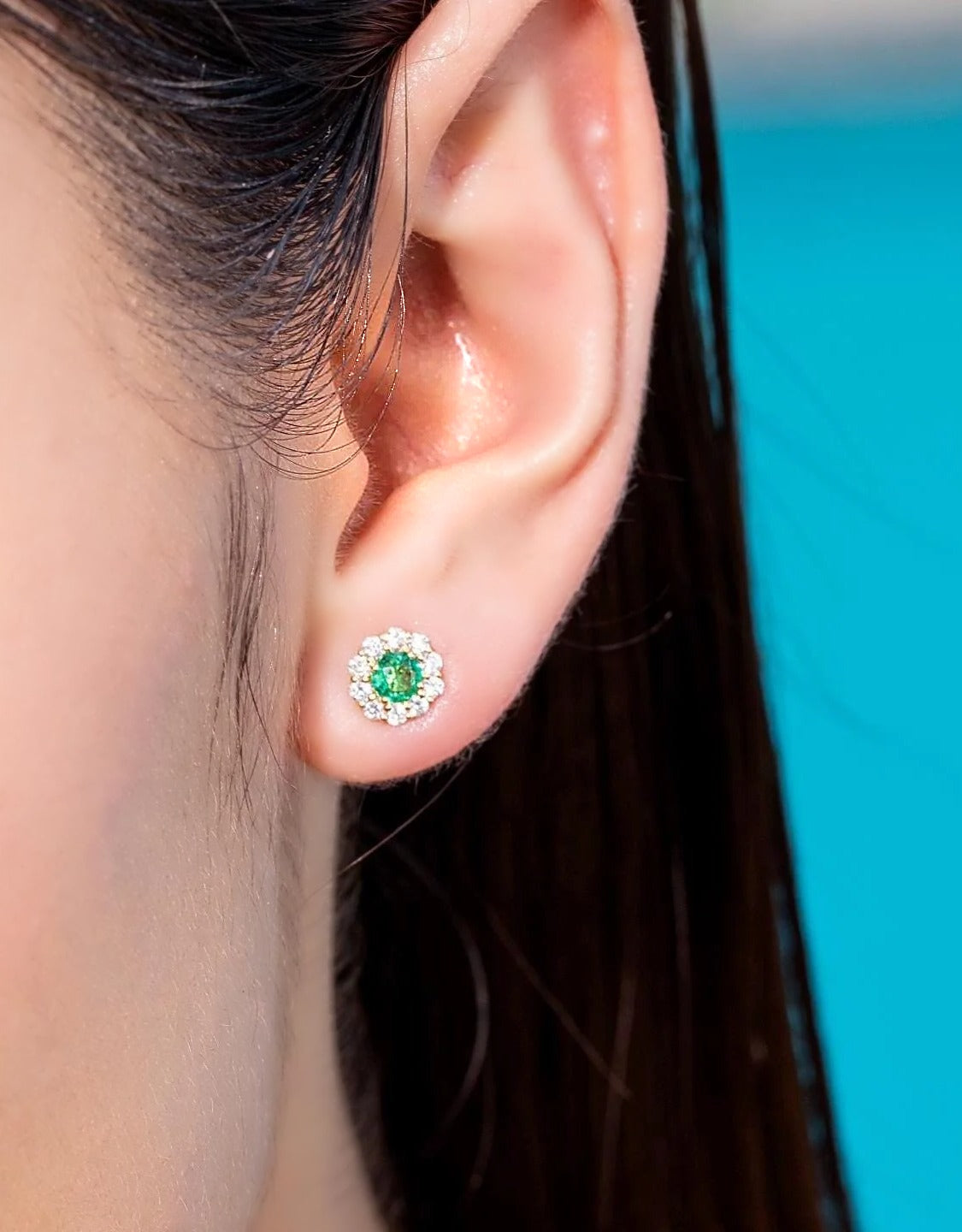 Zambian emerald and diamond halo stud earring in 18K gold, worn on the ear