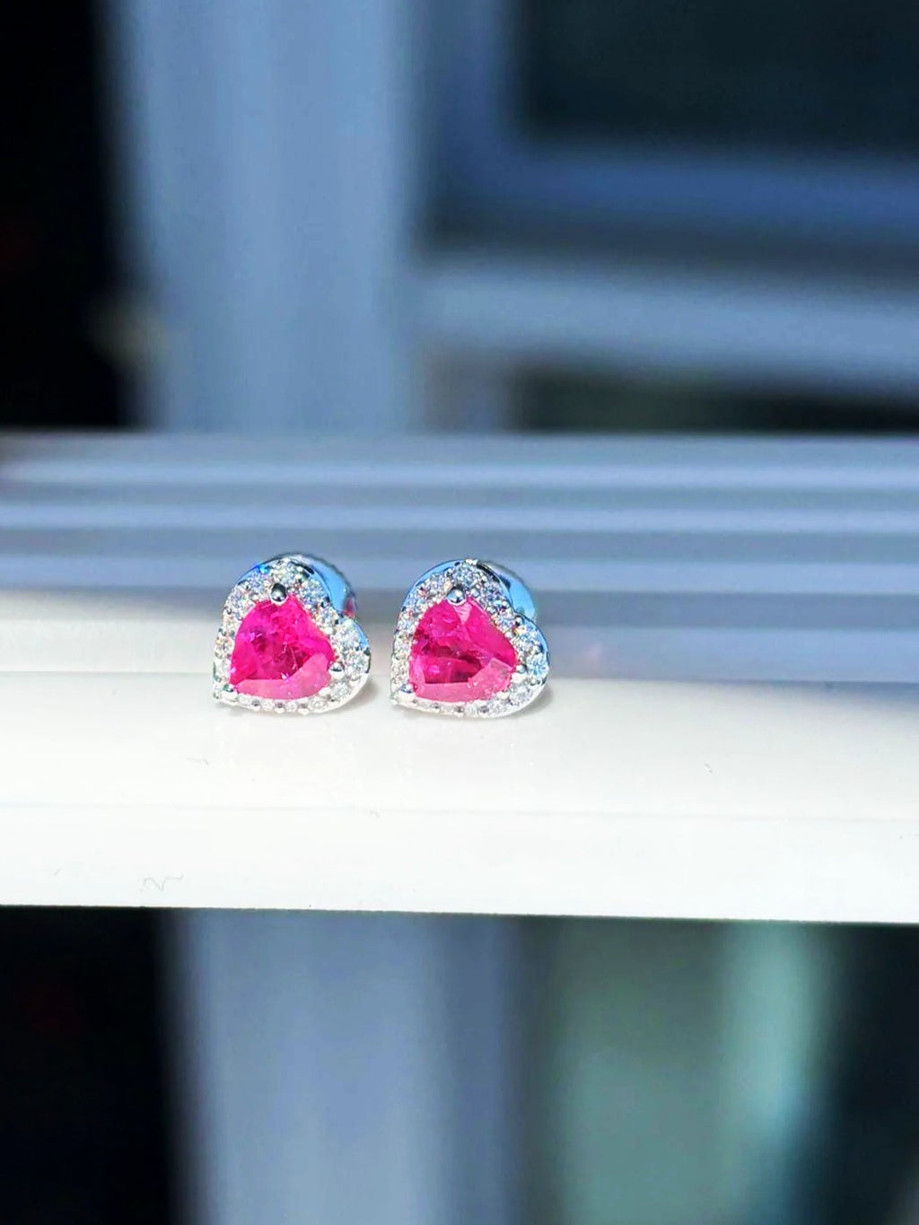 Pink sapphire and diamond heart halo stud earrings in 18K white gold on a white display stand