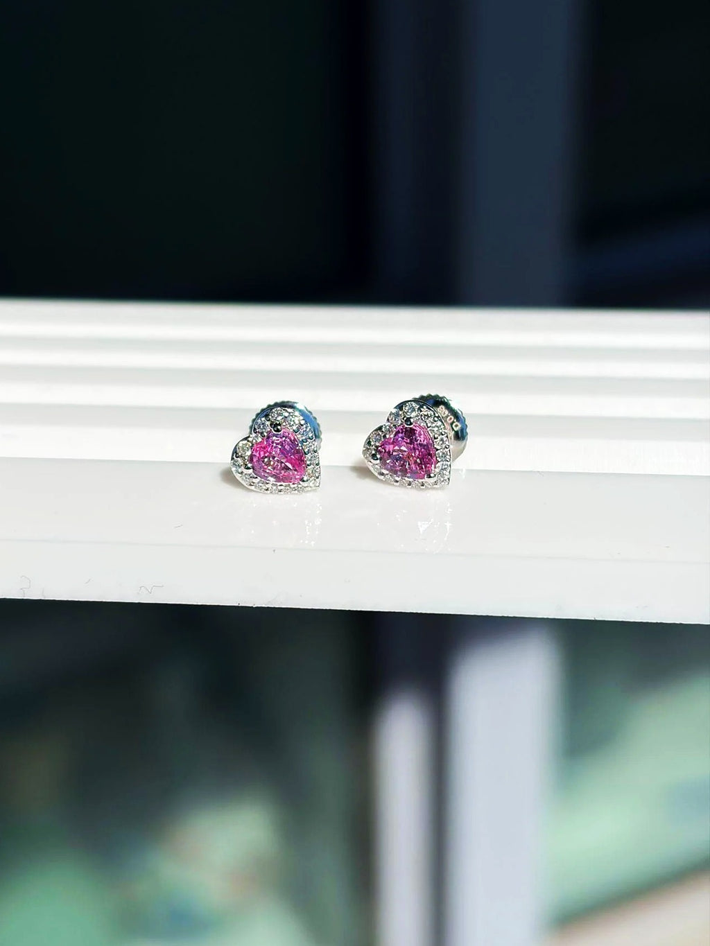 Pendientes de botón pequeños de corazón con zafiro rosa y diamantes en oro blanco de 18K sobre un expositor blanco