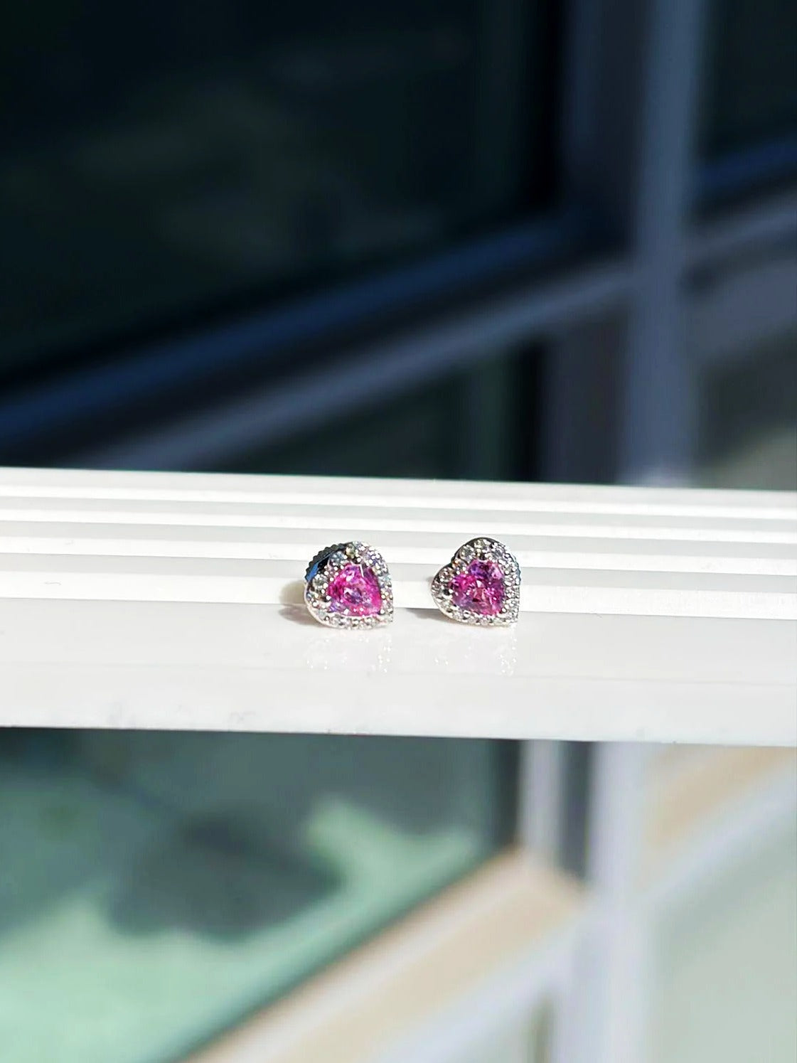 Pendientes de botón pequeños de corazón con zafiro rosa y diamantes en oro blanco de 18K sobre un expositor blanco