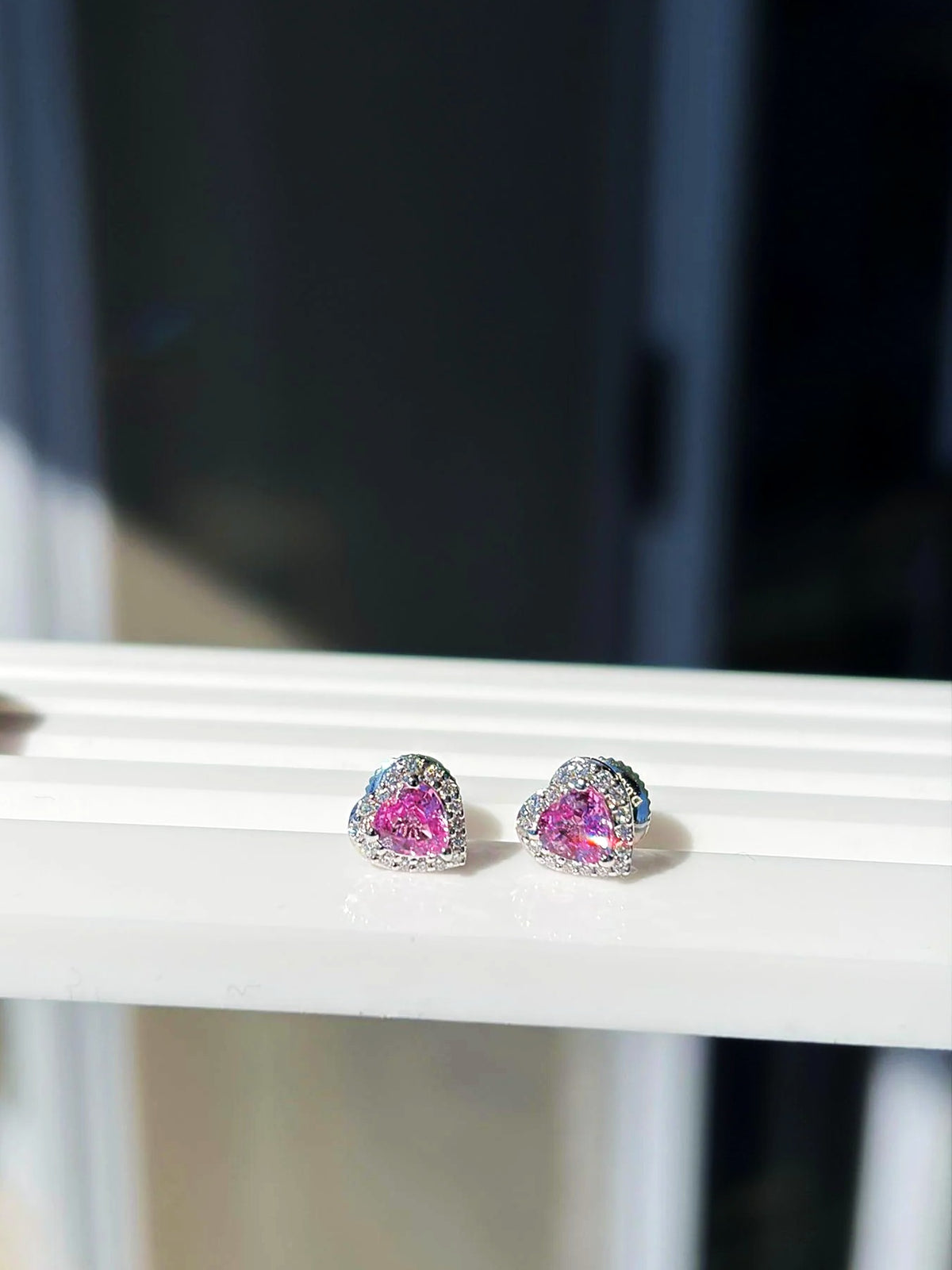 Pendientes de botón pequeños de corazón con zafiro rosa y diamantes en oro blanco de 18K sobre un expositor blanco