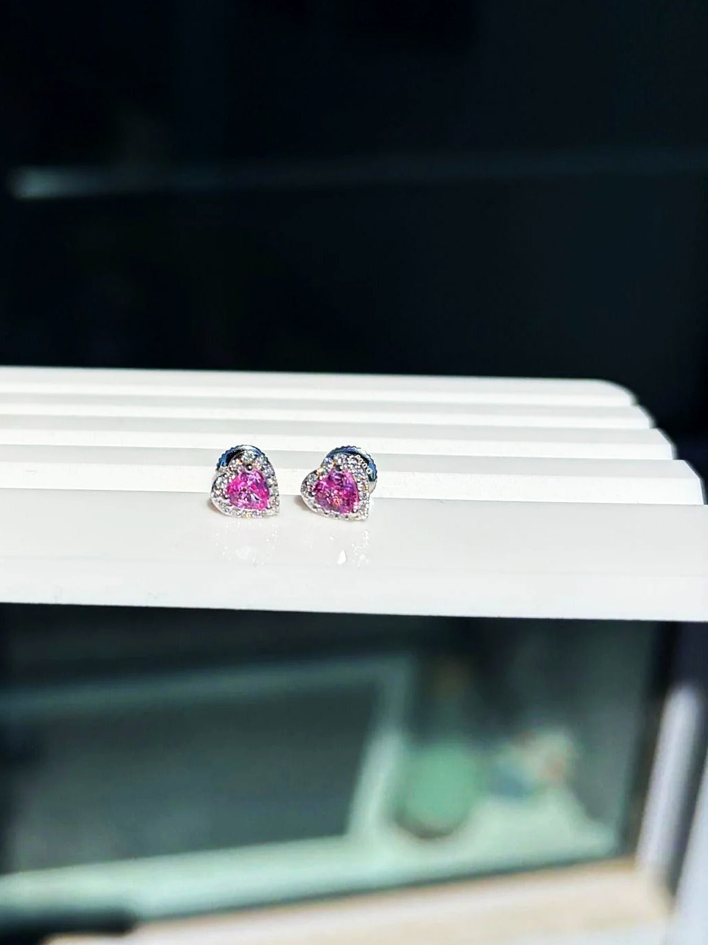 Small pink sapphire and diamond heart stud earrings in 18K white gold on a white display stand