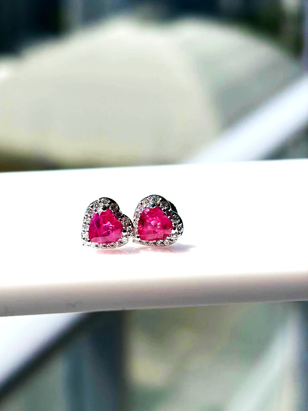 Pink sapphire and diamond heart halo stud earrings in 18K white gold on a white display stand
