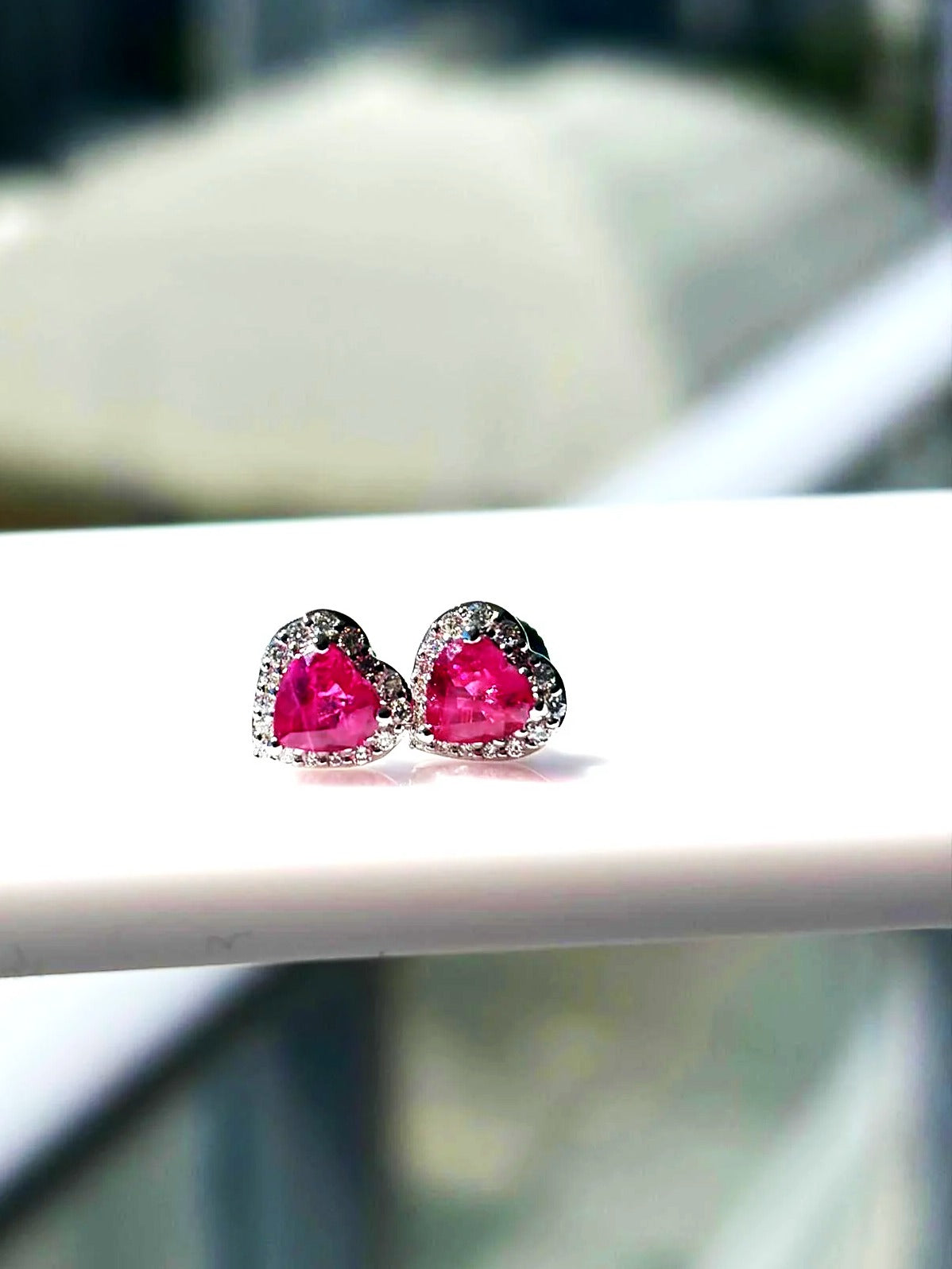Pink sapphire and diamond heart halo stud earrings in 18K white gold on a white display stand