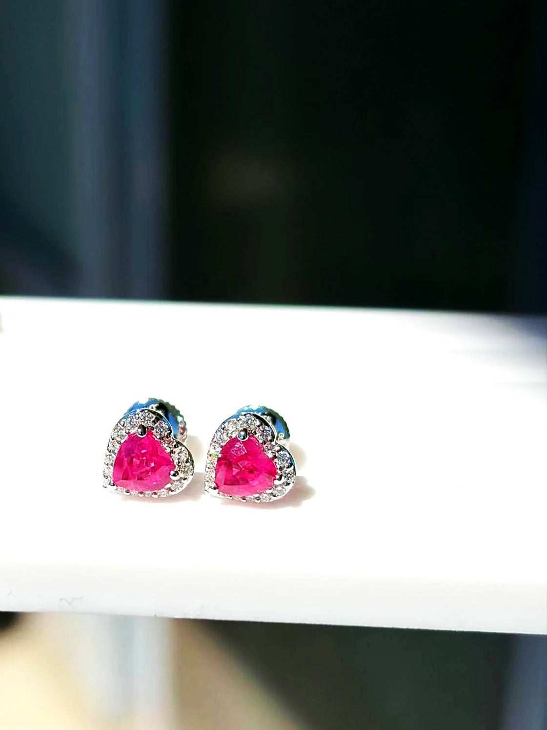 Pink sapphire and diamond heart halo stud earrings in 18K white gold on a white display stand