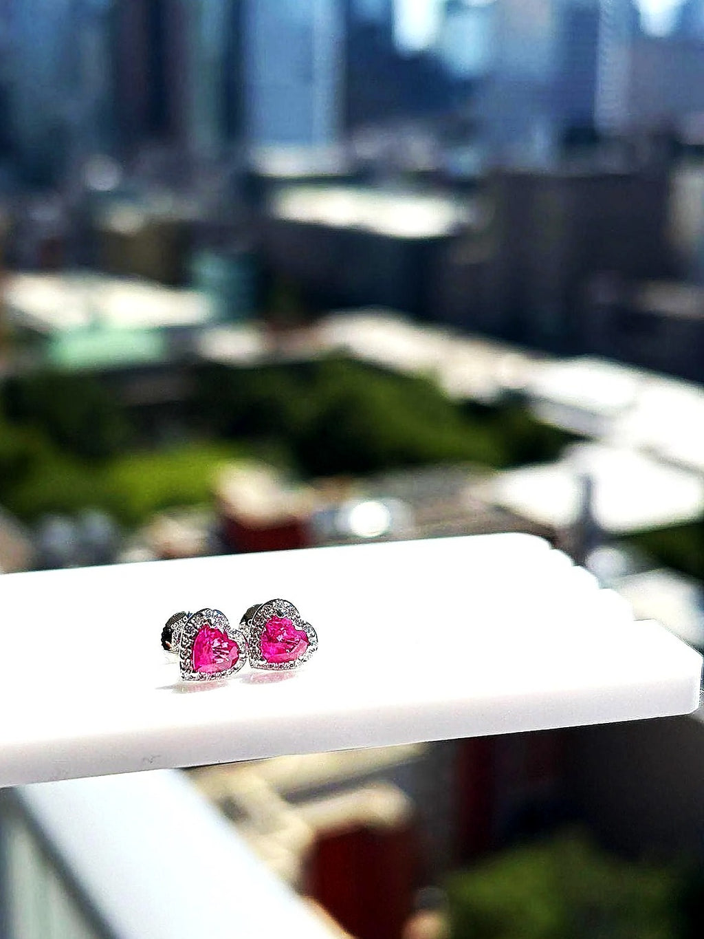 Pink sapphire and diamond heart halo stud earrings in 18K white gold on a white display stand
