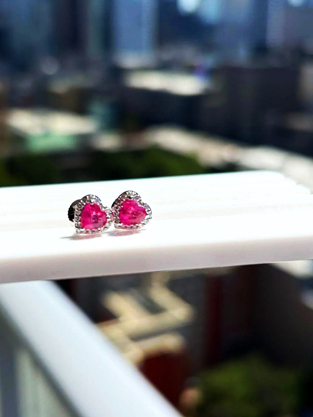 Pink sapphire and diamond heart halo stud earrings in 18K white gold on a white display stand